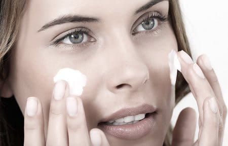 Mujer aplicándose crema en las mejillas