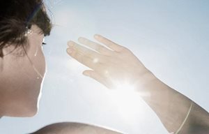 Mujer protegiéndose los ojos del sol con su mano derecha.