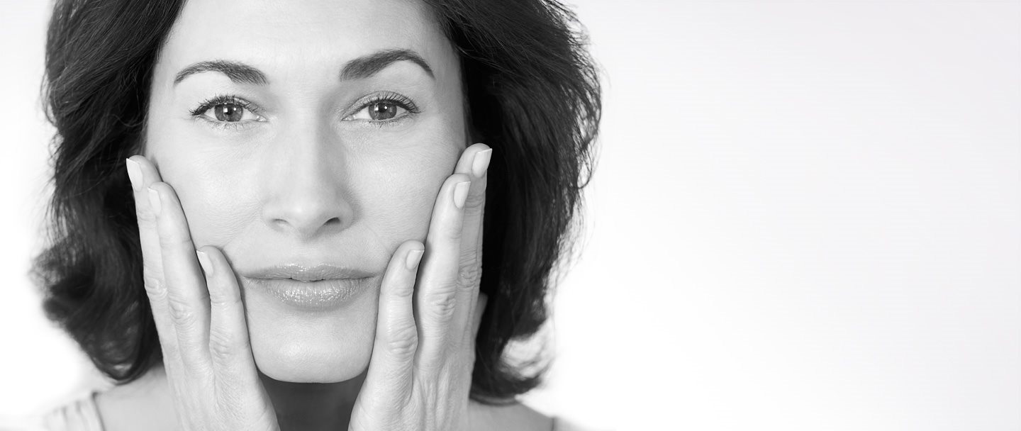 Mujer de mediana edad tocándose las mejillas con ambas manos.