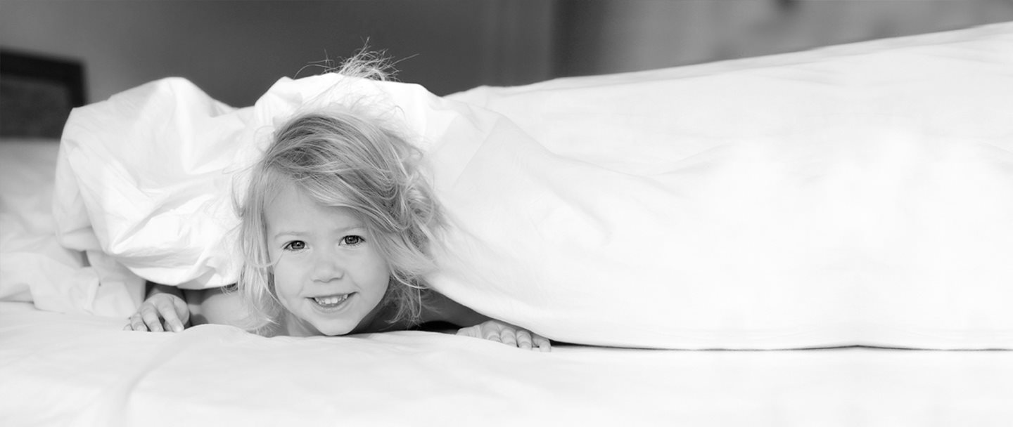 Niña escondida debajo de la sábana de la cama de sus padres